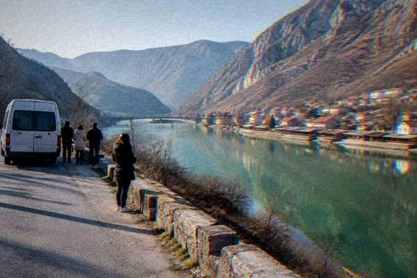 A mountain road beside a milky green lake with bare hills and a small bridge, a minibus stopped at a viewpoint, Jablanica