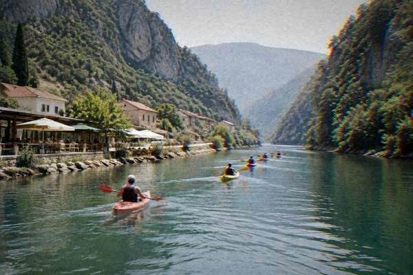 A line of kayaks gliding along a narrow emerald river between steep wooded canyon walls, Jablanica