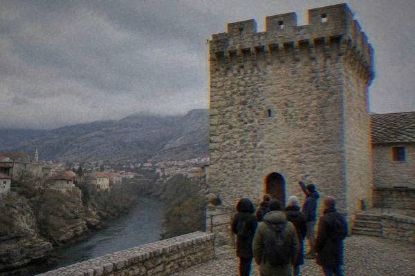 A small group with a guide at the foot of a tall stone gate tower, looking up at its stone battlements, Old Bridge Museum