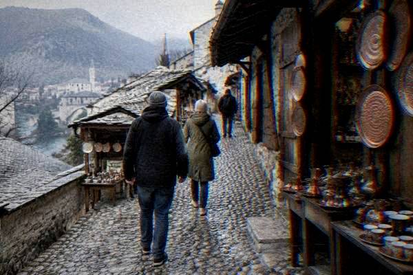 A couple following a guide up a steep pebble-paved lane lined with low stone shops and hanging copper trays, Kujundziluk