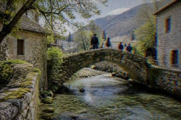 A small group crossing a tiny single-arch stone footbridge over a stream, mossy stone parapets either side, Crooked Bridge