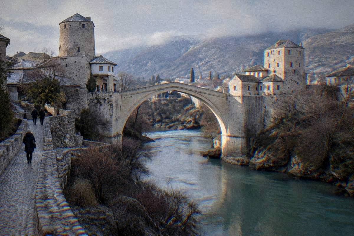 The Neretva river and a single very high pointed arch of pale limestone blocks over a narrow green river gorge between two stone towers bridge in Mostar in winter, grey-green water, Stari Most