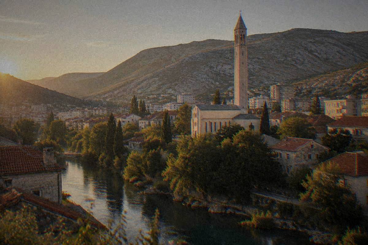 The Franciscan church of Saints Peter and Paul in Mostar, a tall slender pale stone bell tower rising over rooftops and trees, Franjevacka crkva