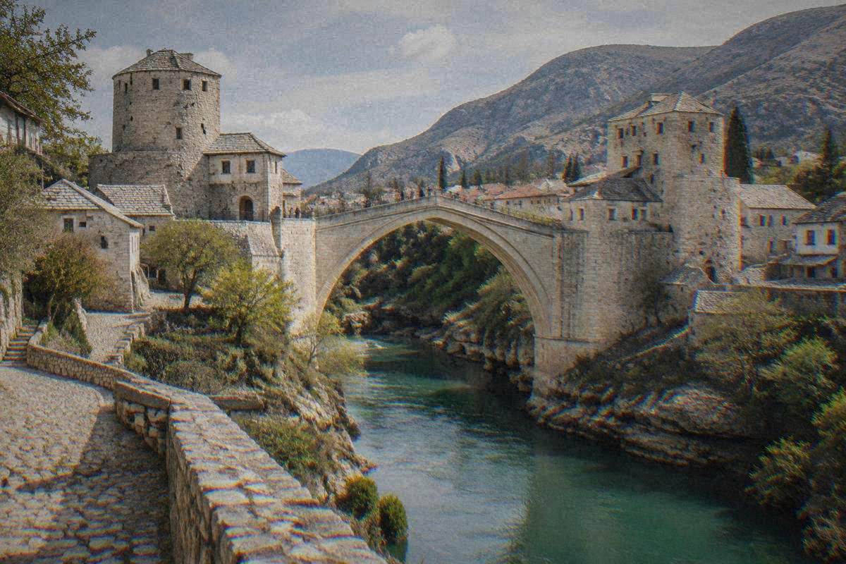 The stone gate tower at the end of a single very high pointed arch of pale limestone blocks over a narrow green river gorge between two stone towers bridge in Mostar, Stari Most