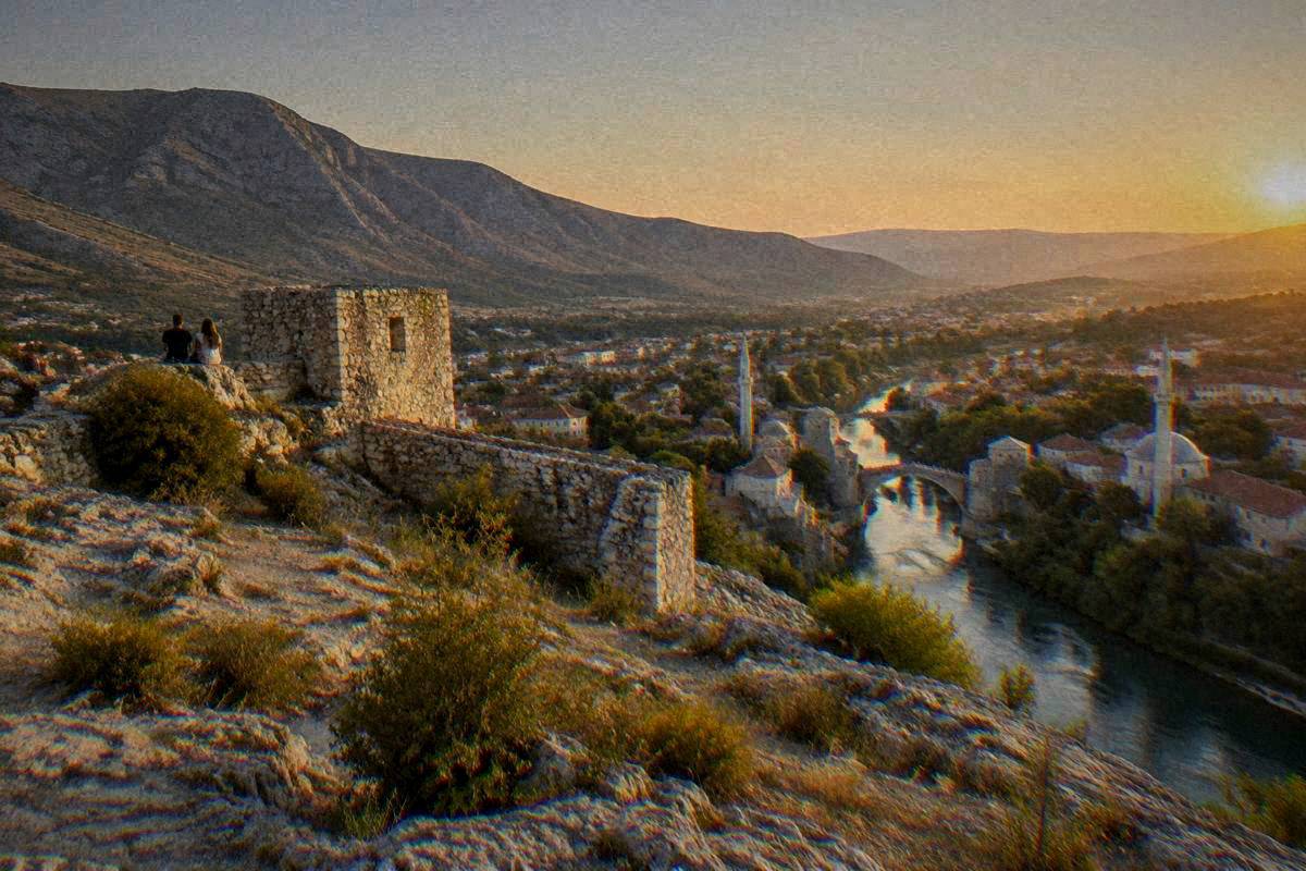 The Fortica hilltop above Mostar at golden hour, bare rock and old stone walls with the town and river valley glowing far below