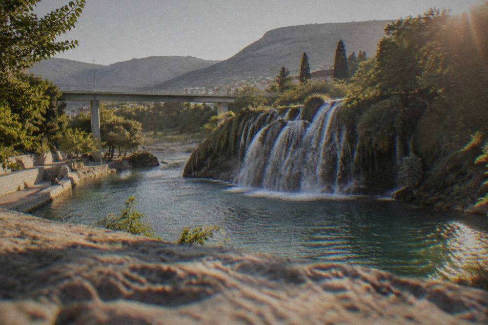 A wide tufa waterfall curving into a natural swimming pool surrounded by trees