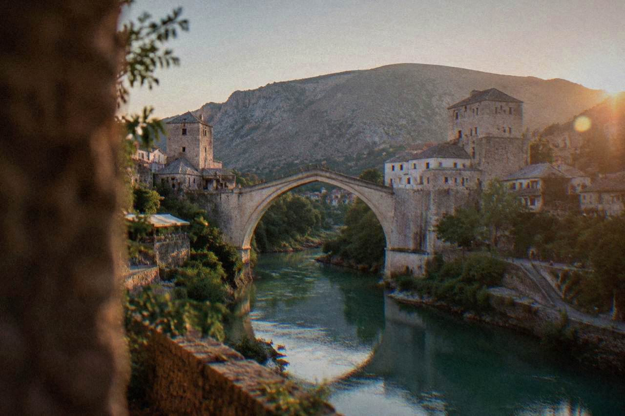 The rebuilt stone Old Bridge arching over the green Neretva river in Mostar at dusk
