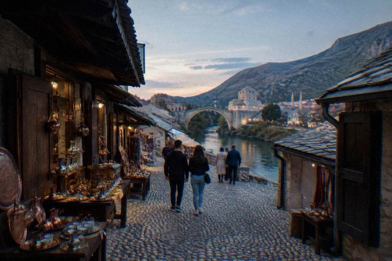 People passing on a cobbled street beside the Neretva river in Mostar's old bazaar