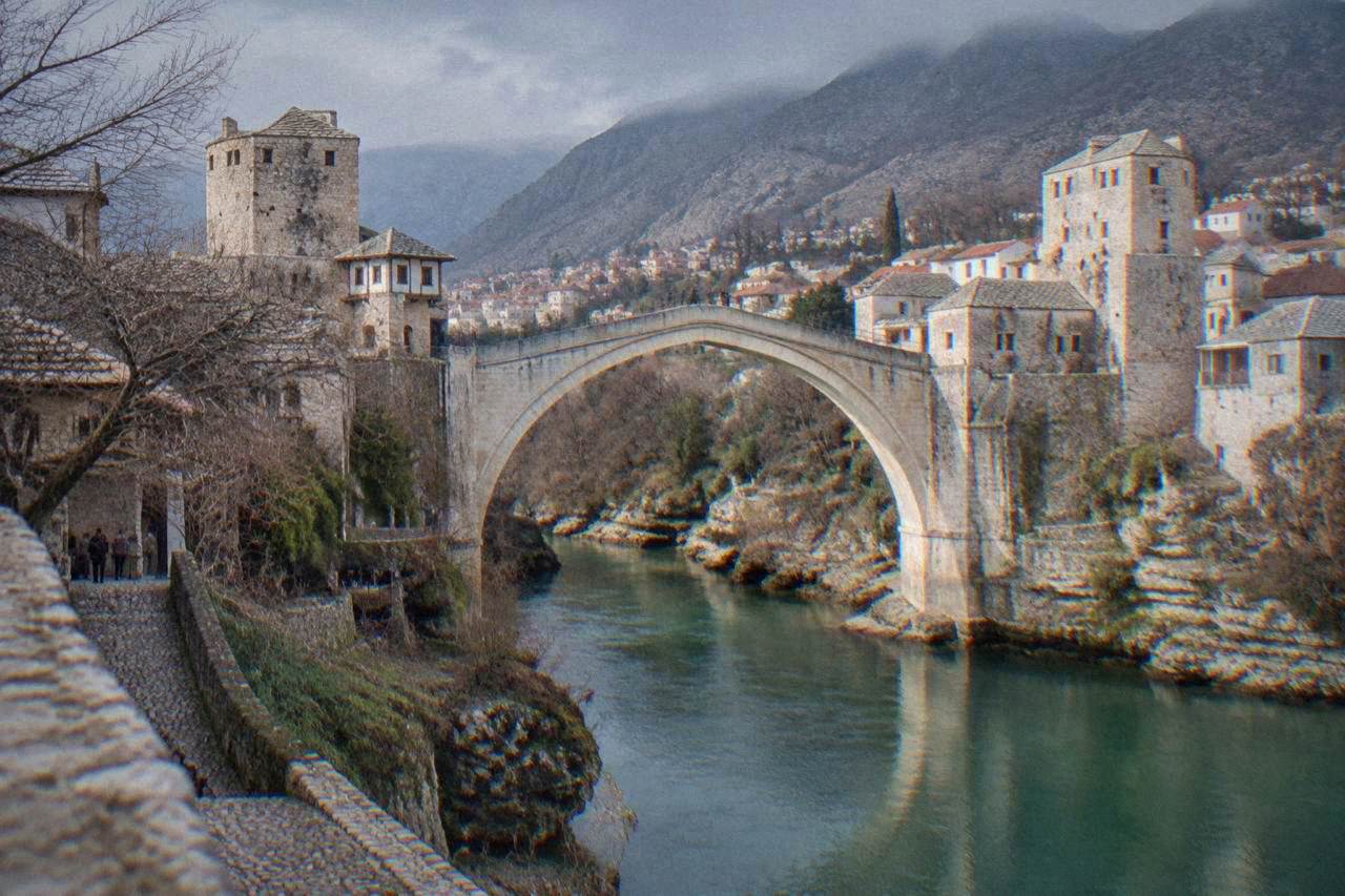 The Old Bridge in Mostar rising over the green Neretva river with stone buildings along the bank