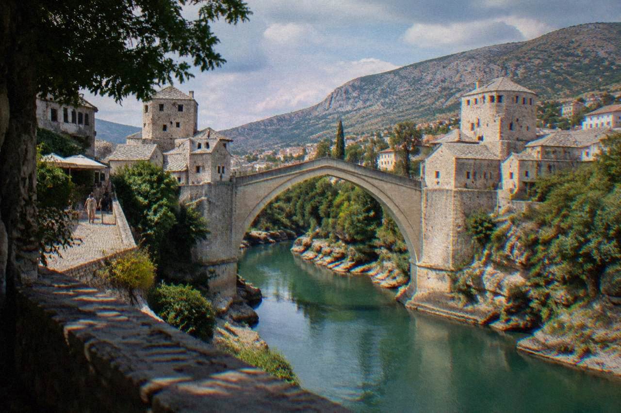 The stone arch of the Old Bridge over the green Neretva river in Mostar at midday