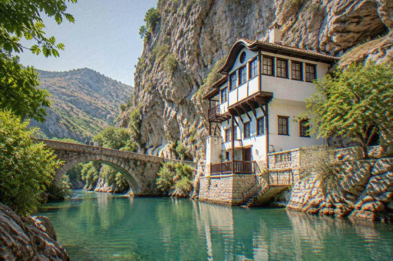A stone footbridge over a turquoise river winding between rocky green hills