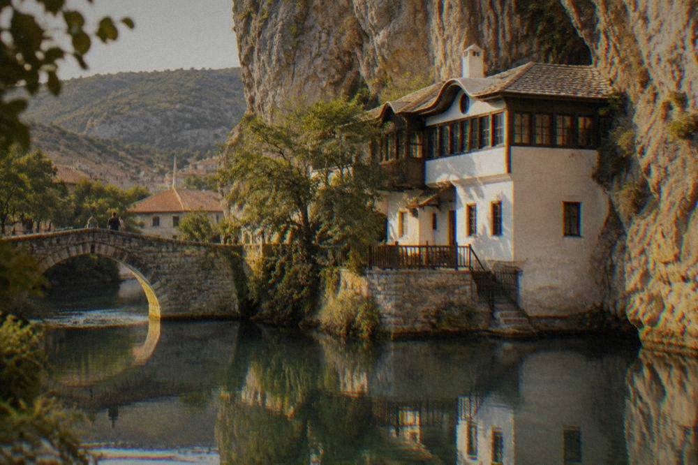 An old stone bridge reflected in a calm river beside a small mountain town