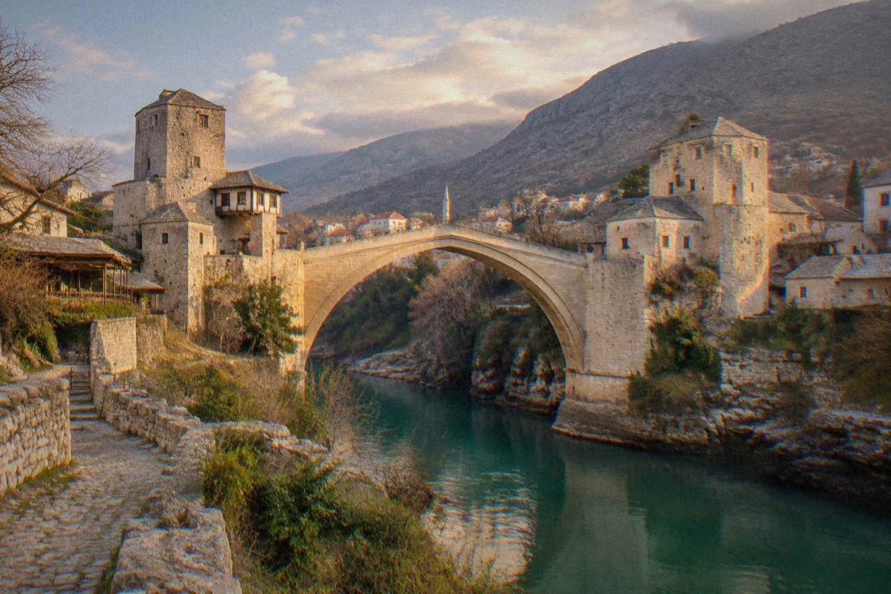 The stone arch of the Old Bridge over the green Neretva river in Mostar at golden hour