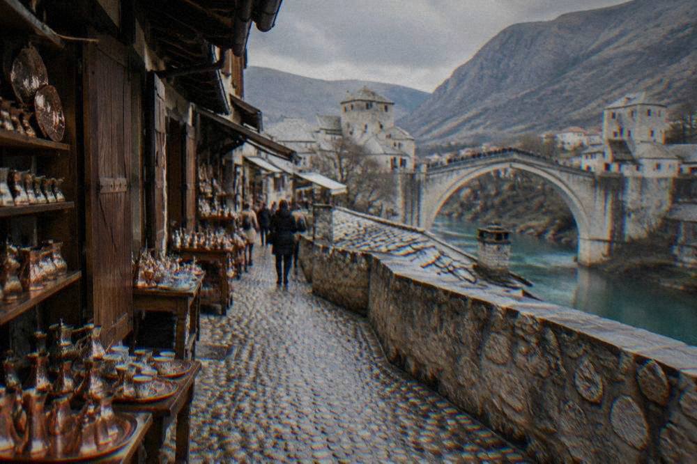 People walking across the rebuilt stone bridge above the cold green river in Mostar's Old Town