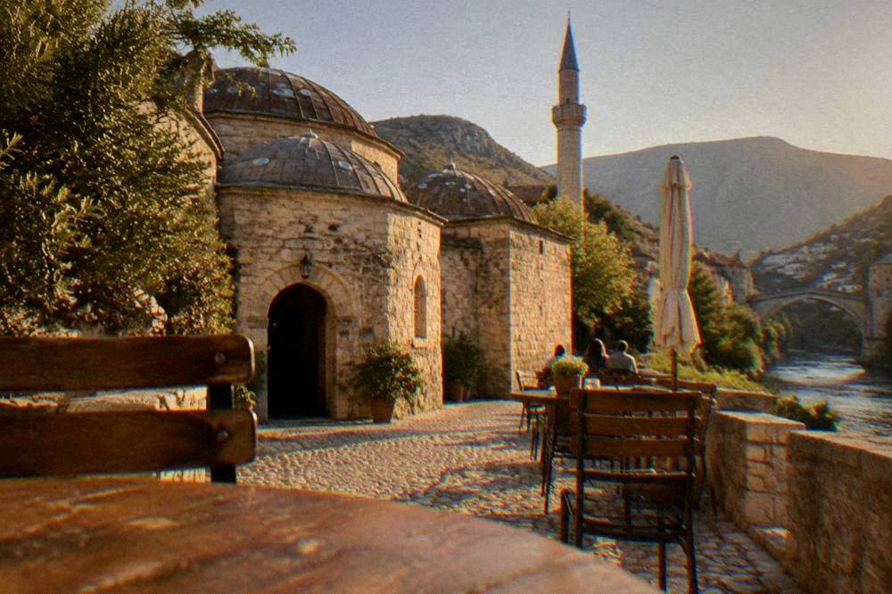 Cafe tables on a stone street near the river with the minaret of the old mosque above
