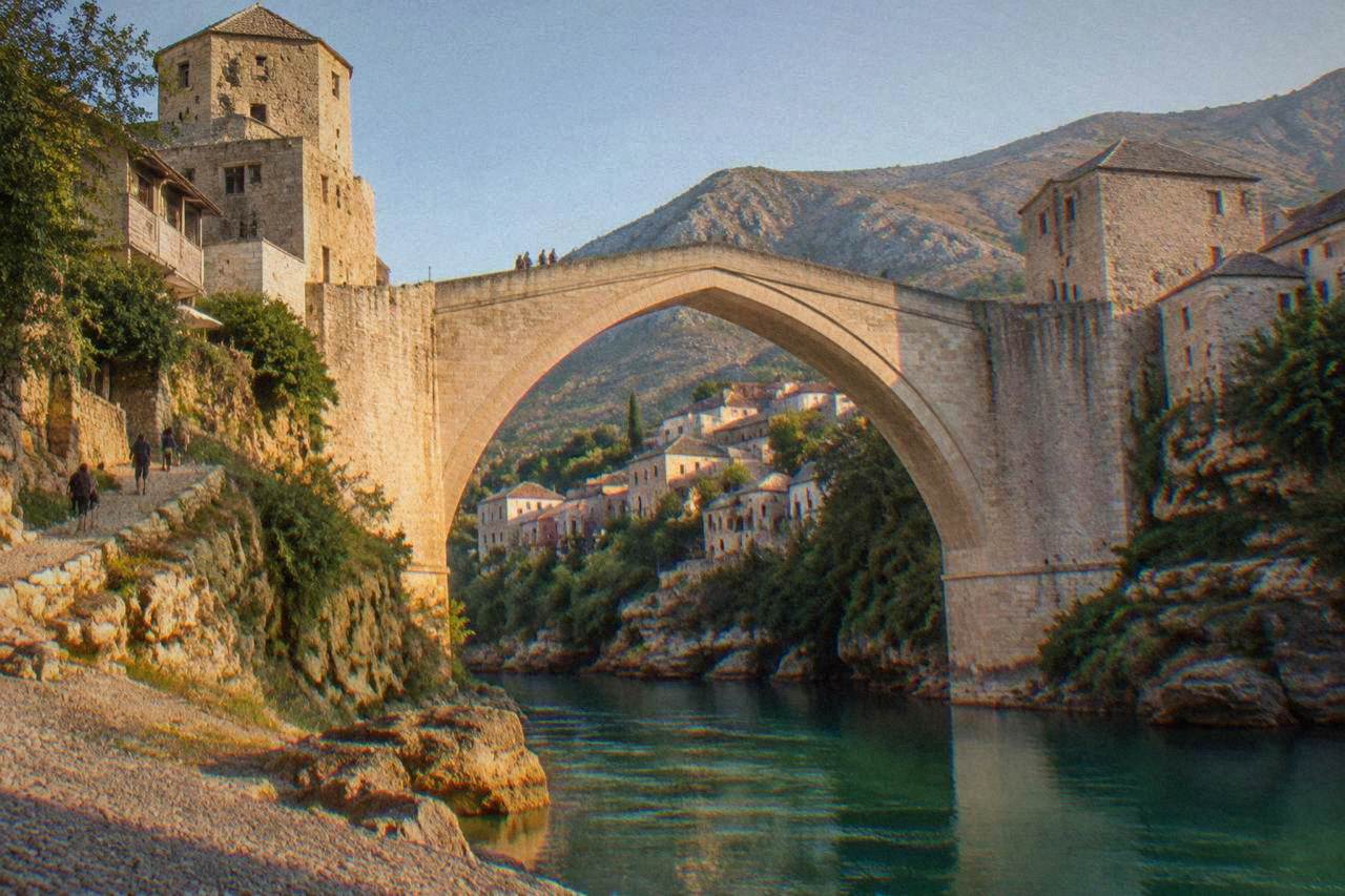 The Old Bridge arching over the green Neretva river with stone buildings of the Old Town behind it