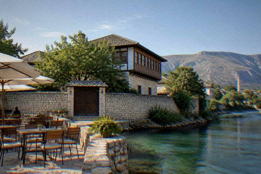 Café terrace beside a stone riverbank with green water flowing past in the morning light