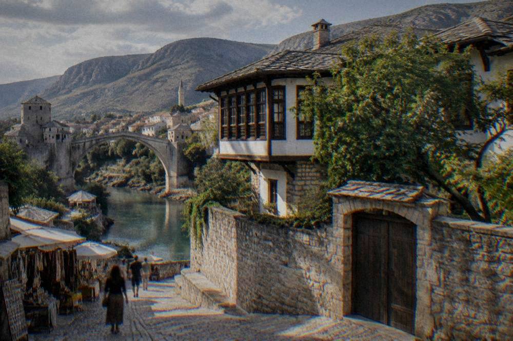 Old stone bridge arching over a green river with a cobbled street and market stalls nearby