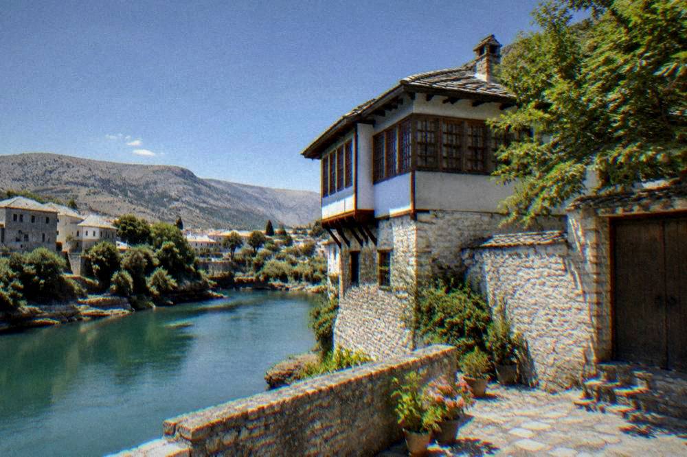 Turquoise river seen from a low stone terrace beneath old house walls in Mostar