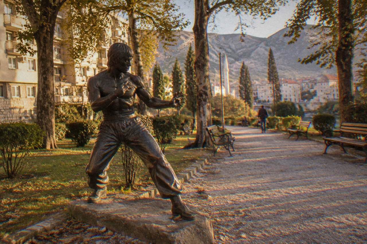A bronze statue of Bruce Lee in fighting stance in a small green park in central Mostar