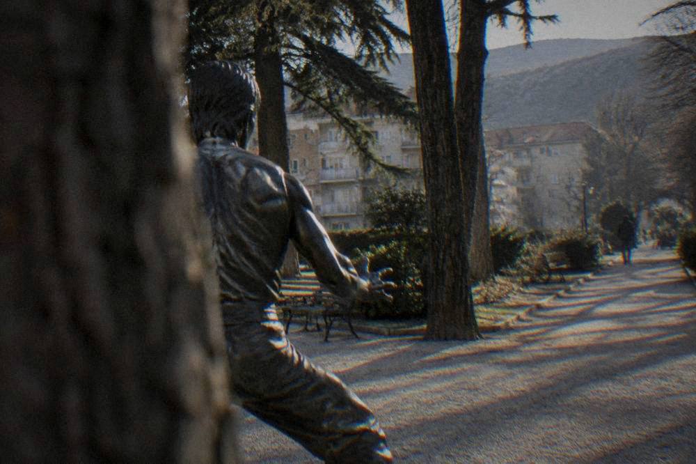Close view of the bronze Bruce Lee statue with trees and park benches behind it