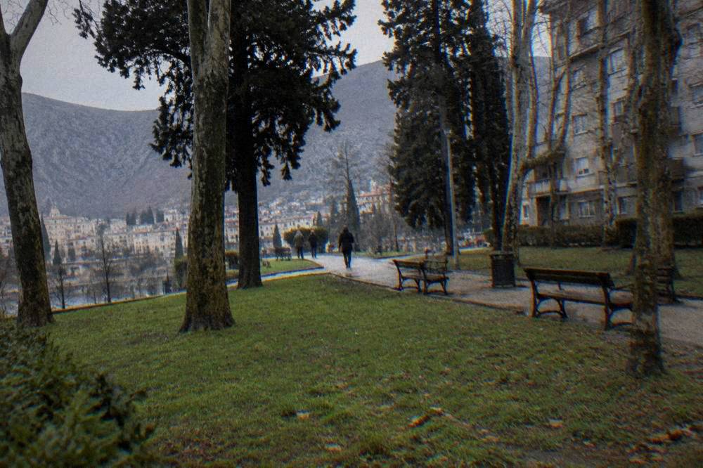 The Bruce Lee statue seen from a distance across a grassy park in the centre of Mostar