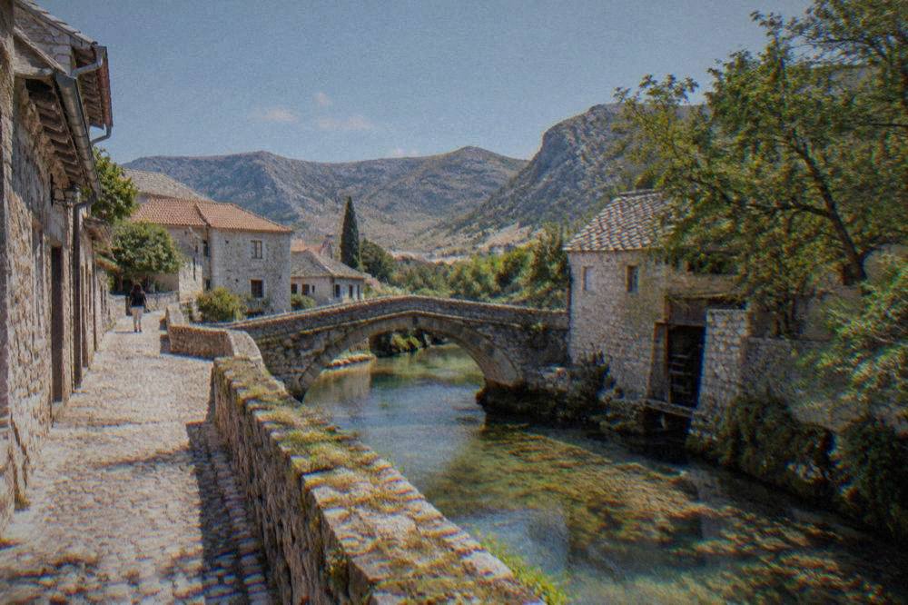 A narrow cobbled lane with old stone houses leading toward a small stone bridge