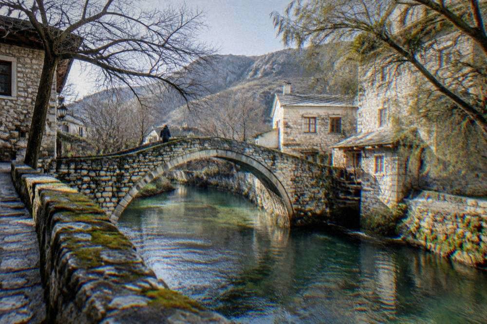 A gentle stone bridge over a small green river with stone embankments on both sides