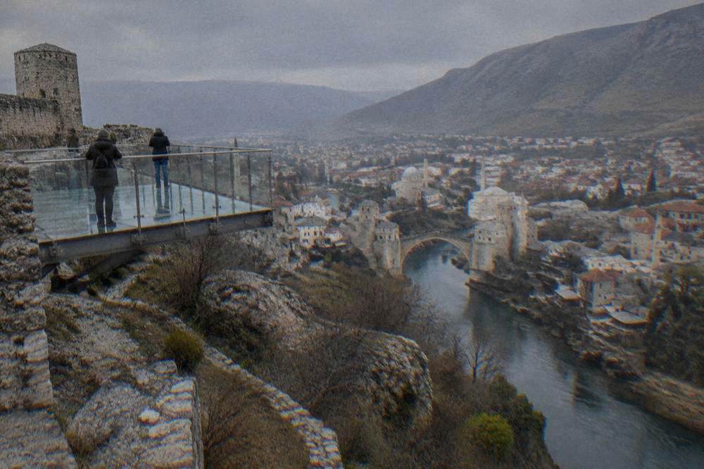 Glass-floored viewing platform extending over a cliff edge with a panoramic town view