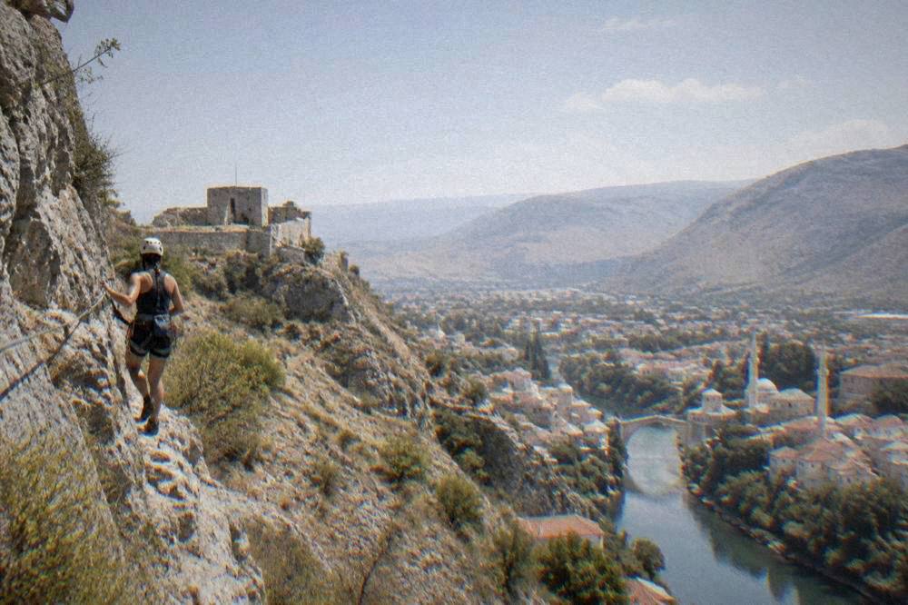 Climber in helmet and harness attached to a steel cable on a limestone cliff face