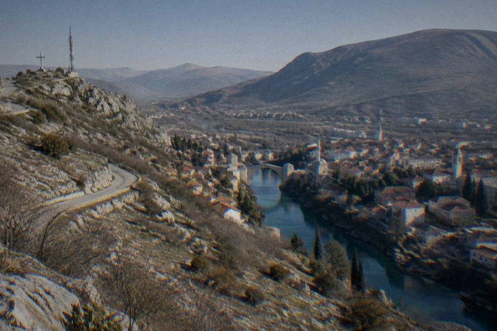 Red rooftops, church towers and minarets of a river city seen from a high rocky viewpoint in clear weather