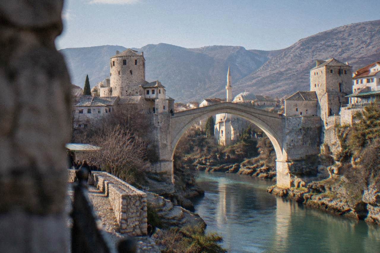 Stone mosque with a slender minaret standing beside the turquoise Neretva river below the Old Bridge in Mostar