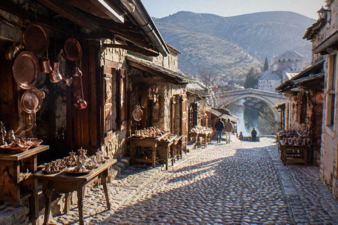 A narrow cobbled bazaar street lined with small stone shops and hanging copper goods leading toward a stone bridge