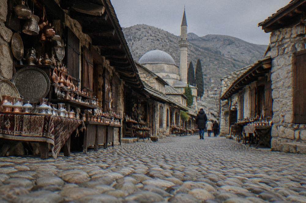 Cobbled lane in the Old Town of Mostar with stone walls and a domed roof behind
