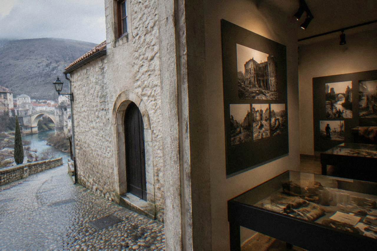 A quiet museum interior with display panels and personal objects from the 1992 to 1995 war lit under soft spotlights