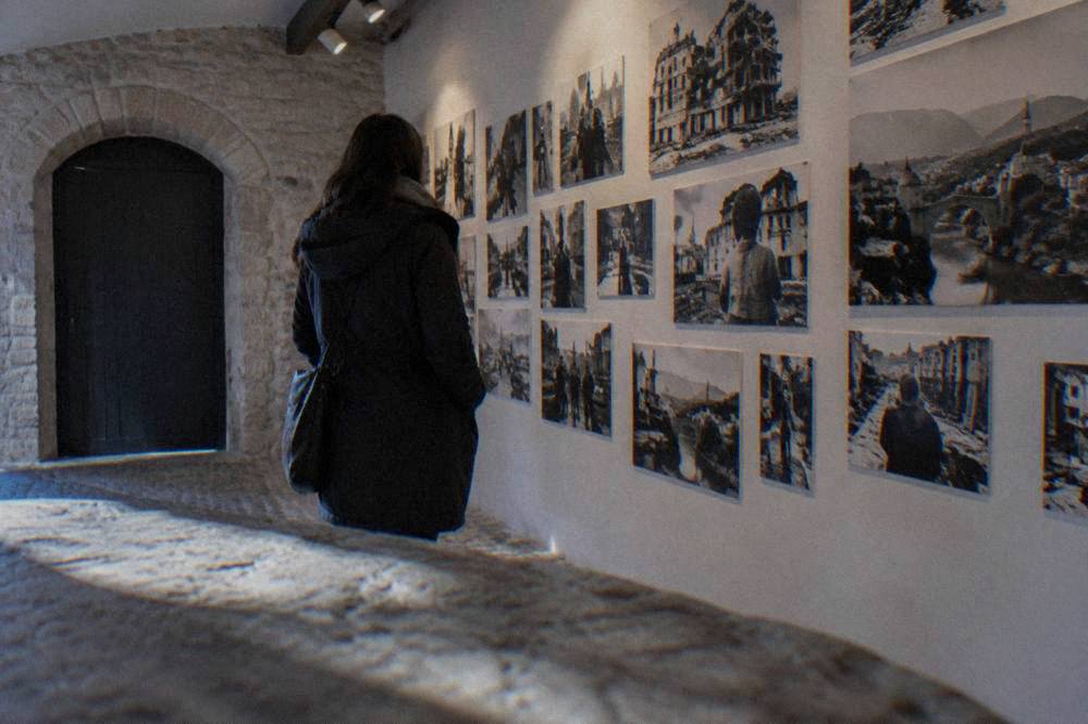 A visitor reading a wall of photographs and names inside a small war documentation museum