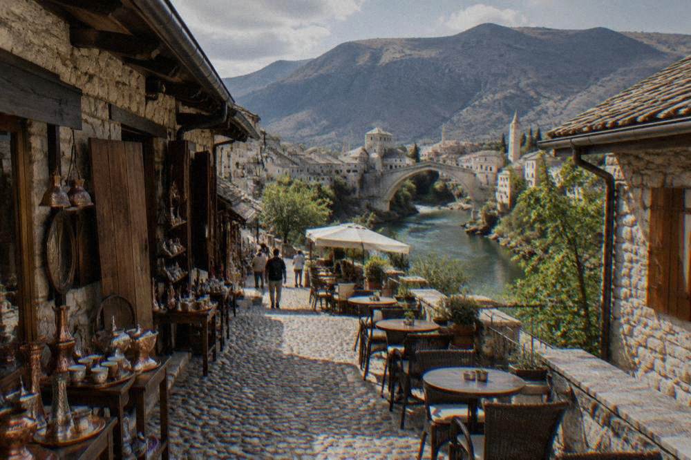 A stone street in central Mostar with cafe tables leading toward the Neretva river