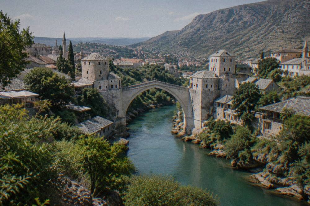 The Old Bridge and the Neretva river seen from a green hillside above Mostar at midday