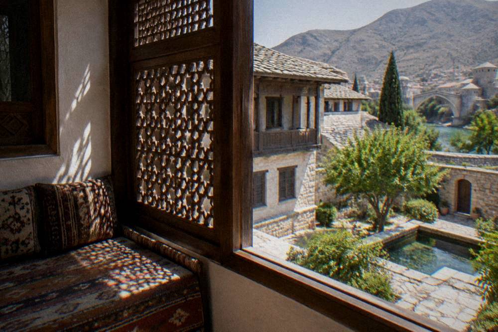Carved wooden screen and window of an Ottoman upper room with light falling on a low sofa