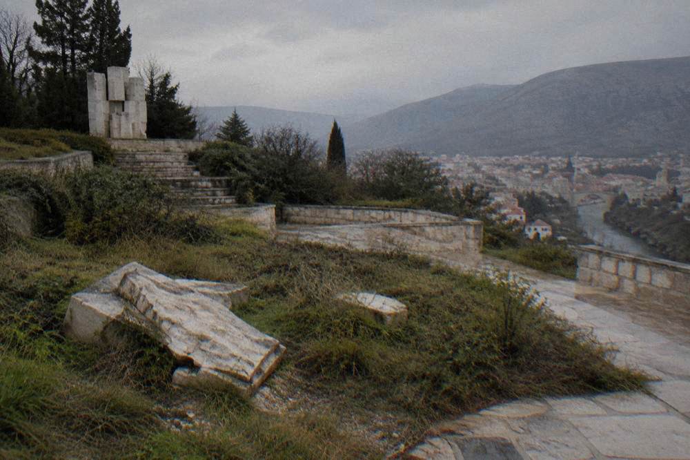 Broken carved stone markers lying on an overgrown terrace of a memorial site