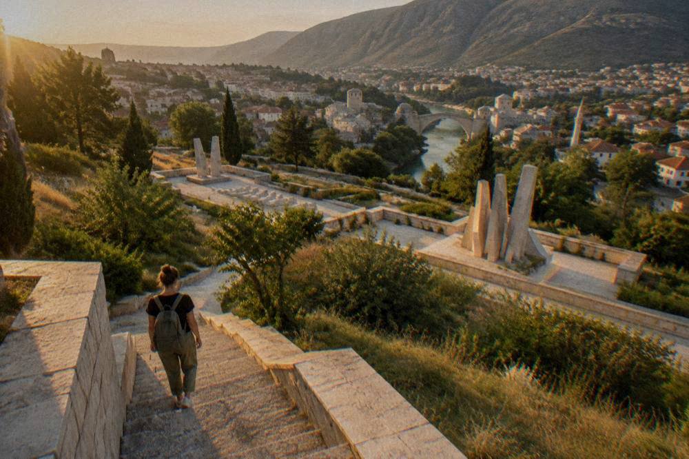 A visitor in walking shoes pausing on a stone stair between memorial terraces