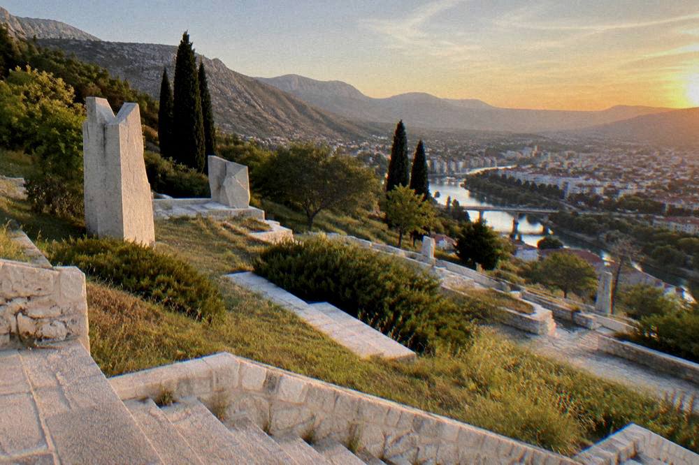 Sunset over a terraced stone memorial with a river valley city beyond