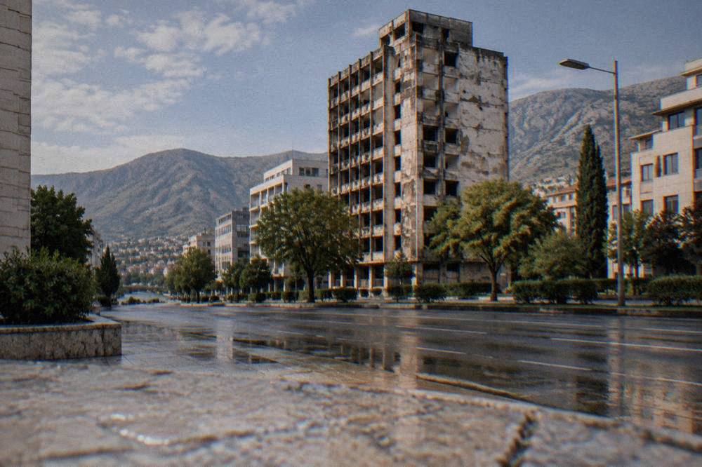 The graffiti-covered lower floors of a ruined concrete tower seen from a street corner in Mostar