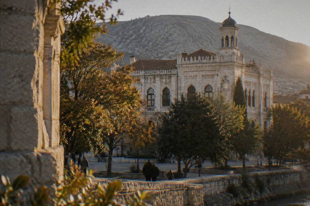The stone facade of the Old Gymnasium building beside a city square in Mostar