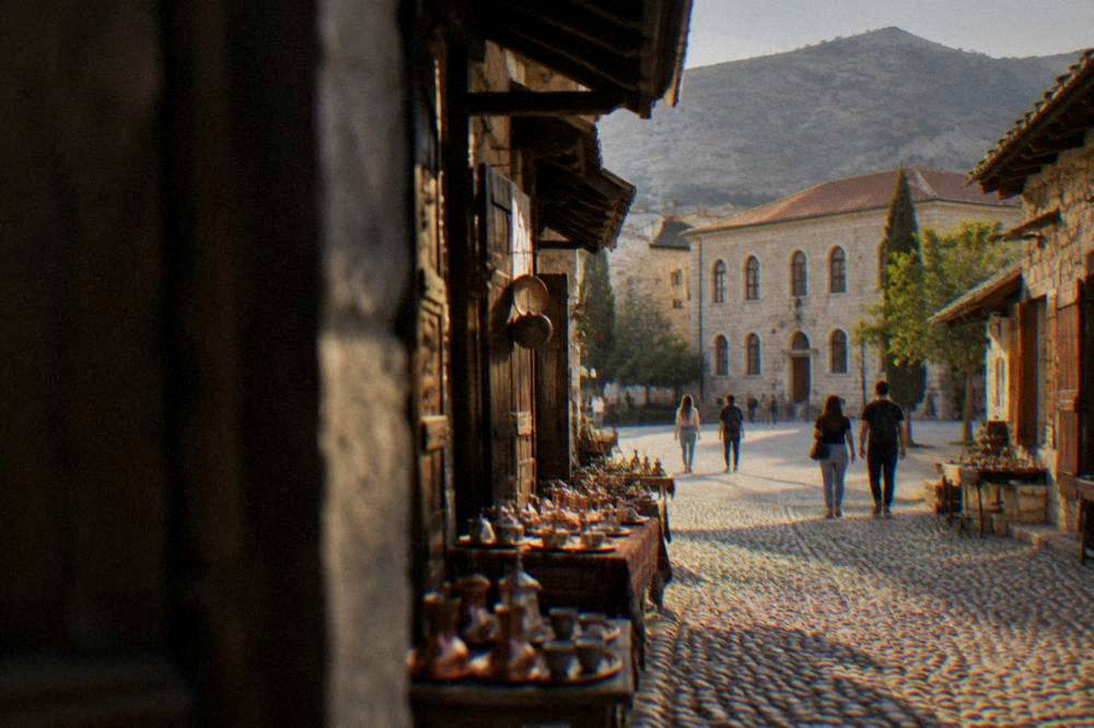 Students and pedestrians crossing a paved square in front of a historic school building in Mostar