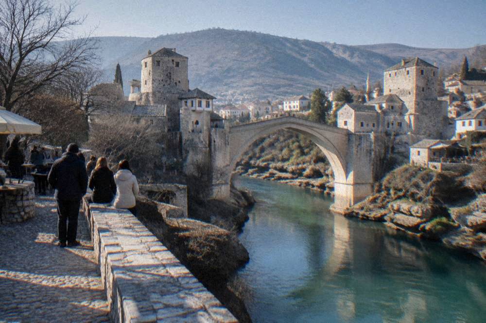 A diver in mid-air between a stone bridge and a deep green river below
