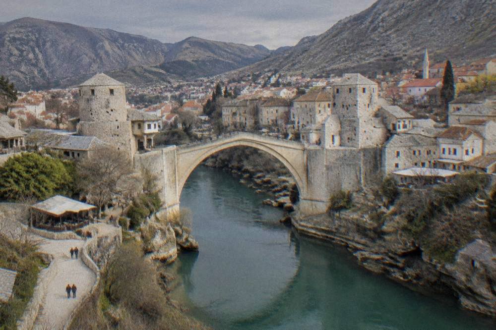 A wide view of an old city with a stone bridge and a river cutting between hills