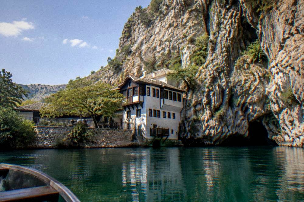 The cliff and dervish lodge seen from a small boat on dark green water