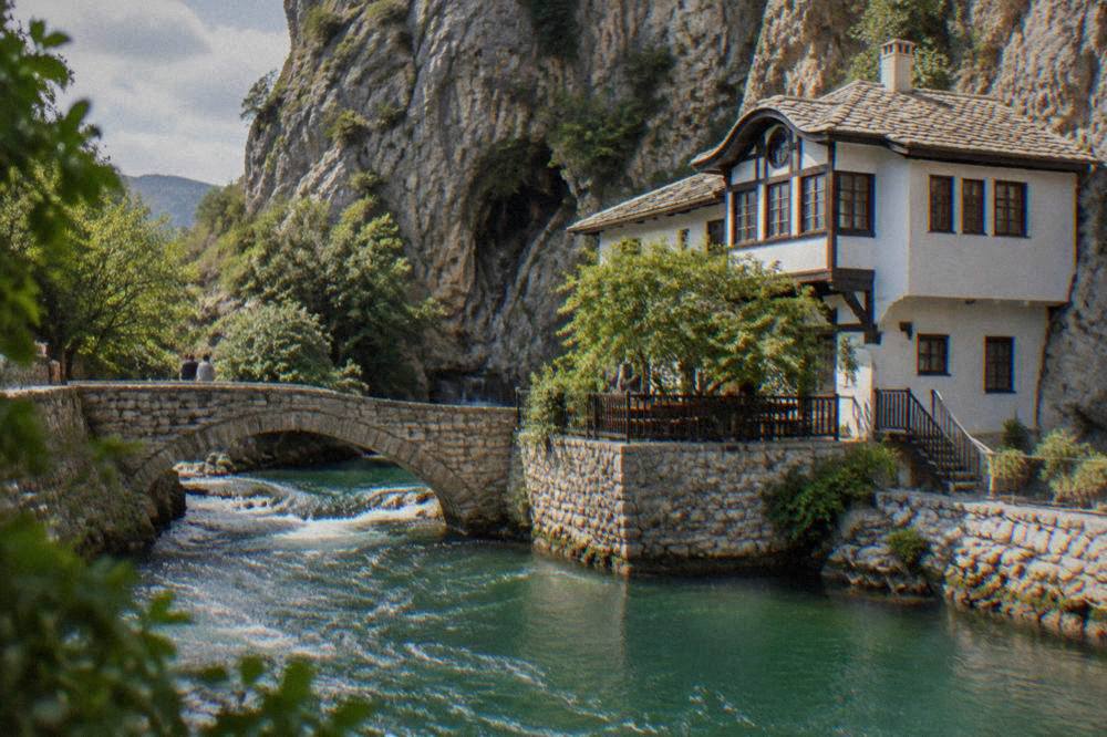 Fast green river water flowing under a small stone bridge below steep cliffs