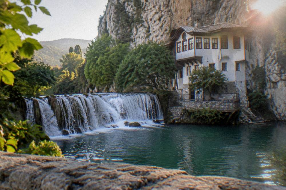 A wide waterfall curving around a green pool ringed by trees